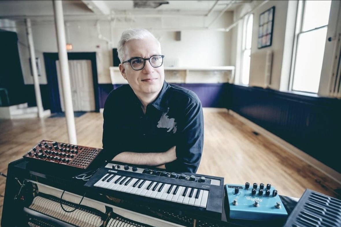 Musician leaning on a piano keyboard in a studio.