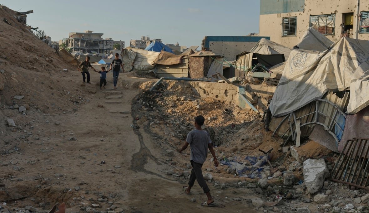 A few individuals navigating through a damaged neighborhood, using fabric to create makeshift shelters over ruined buildings.