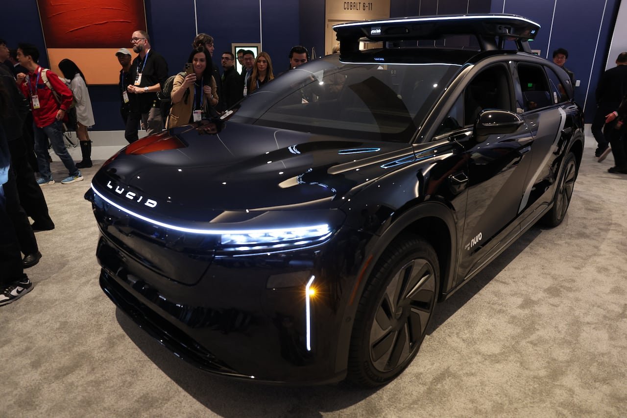 default-210 Robotaxi vehicle branded as Lucid on the front, displayed at a convention center trade show.
